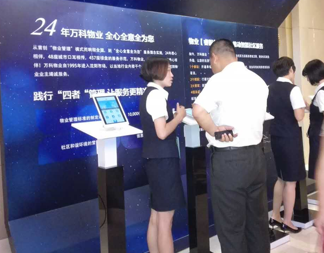 (发布会外场展示区,物业人员正为客户现场演示讲解万科物业"睿服务")